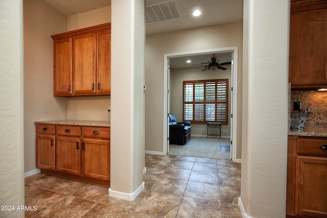 interior space with light tile patterned flooring, decorative backsplash, light stone counters, and ceiling fan