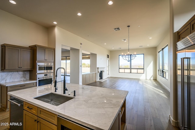 kitchen featuring sink, appliances with stainless steel finishes, light stone countertops, a center island with sink, and beverage cooler