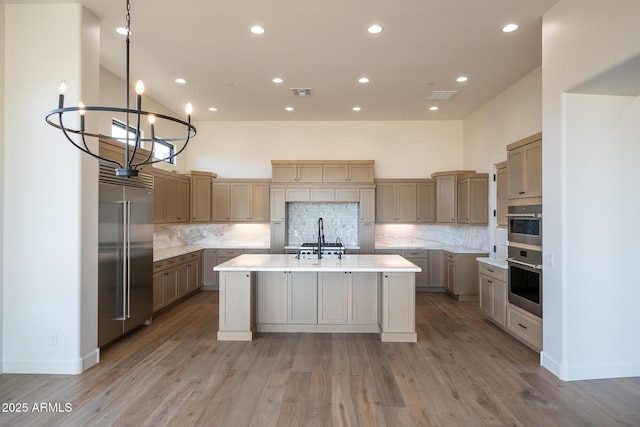 kitchen with hanging light fixtures, light hardwood / wood-style flooring, a center island with sink, built in fridge, and a high ceiling