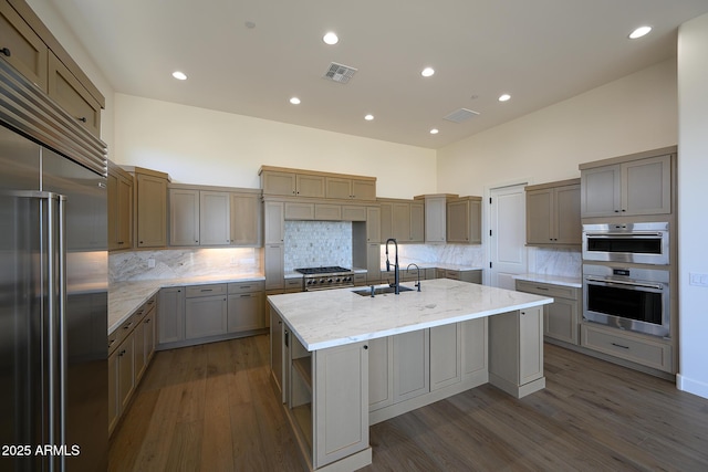 kitchen with dark hardwood / wood-style floors, a towering ceiling, an island with sink, sink, and premium appliances