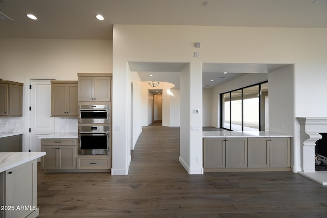 kitchen featuring dark wood-type flooring, stainless steel double oven, decorative backsplash, and a high ceiling