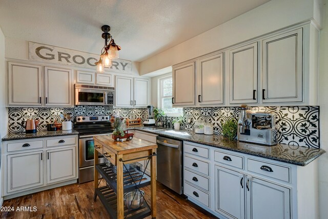 kitchen with decorative light fixtures, appliances with stainless steel finishes, dark hardwood / wood-style floors, and decorative backsplash