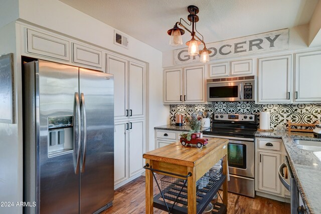 kitchen with light stone counters, stainless steel appliances, tasteful backsplash, dark hardwood / wood-style flooring, and hanging light fixtures