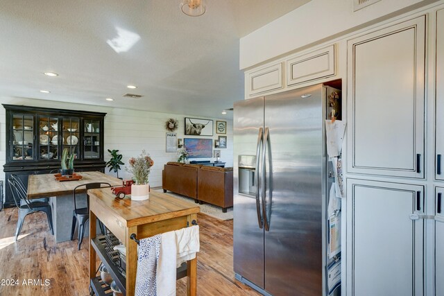 kitchen featuring cream cabinets, light wood-type flooring, a textured ceiling, and stainless steel refrigerator with ice dispenser