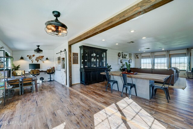 interior space with a kitchen bar, beamed ceiling, a barn door, and wood-type flooring