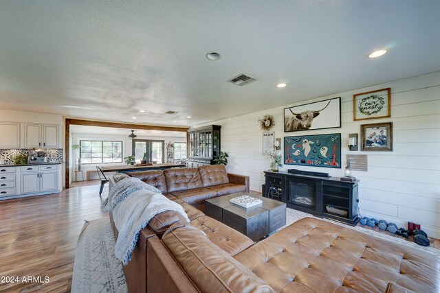 living room with a textured ceiling, wooden walls, and light hardwood / wood-style flooring