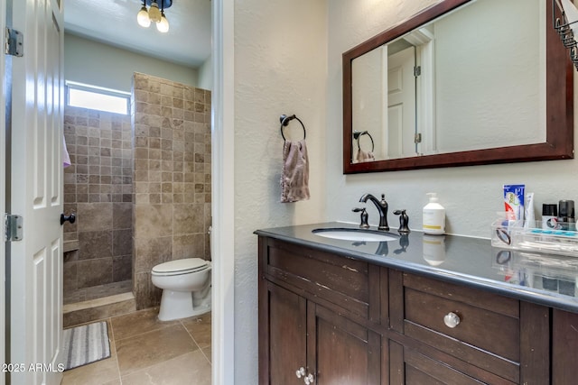 bathroom with toilet, vanity, tile patterned flooring, a textured wall, and a tile shower