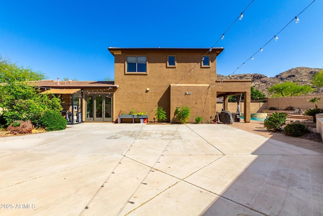 rear view of property featuring a mountain view, stucco siding, fence, and a patio area
