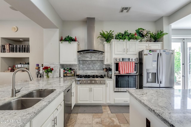 kitchen with light stone countertops, a sink, decorative backsplash, wall chimney exhaust hood, and appliances with stainless steel finishes