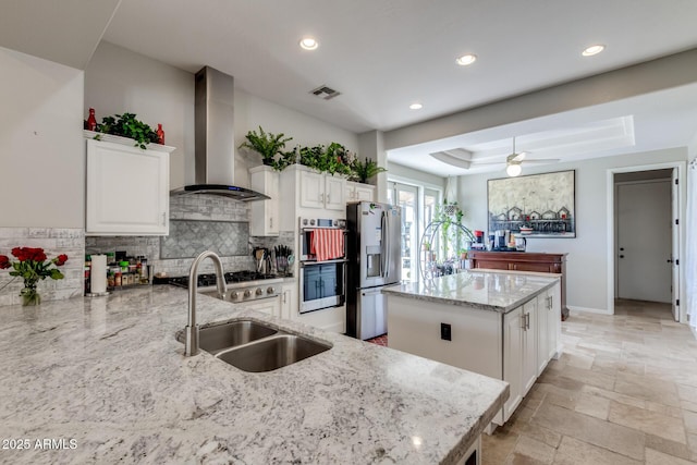 kitchen with a raised ceiling, visible vents, a kitchen island, wall chimney range hood, and stainless steel appliances