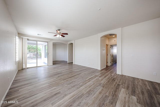 unfurnished room featuring visible vents, wood finished floors, baseboards, ceiling fan, and arched walkways