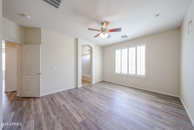 unfurnished bedroom with arched walkways, baseboards, light wood finished floors, and visible vents