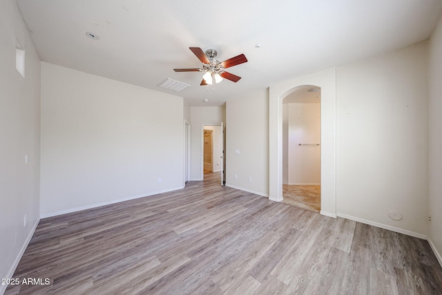 empty room featuring arched walkways, light wood-style flooring, a ceiling fan, baseboards, and visible vents