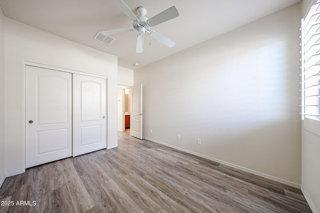 unfurnished bedroom featuring a ceiling fan, baseboards, wood finished floors, visible vents, and a closet