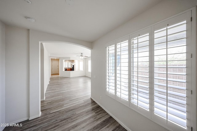 hall featuring arched walkways, baseboards, and wood finished floors