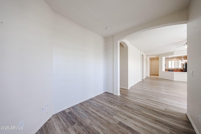 spare room with baseboards, arched walkways, ceiling fan with notable chandelier, and wood finished floors