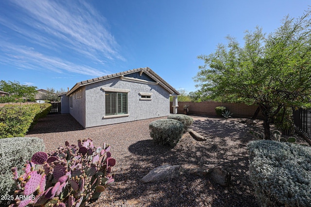 view of side of home with a tile roof, a fenced backyard, and stucco siding