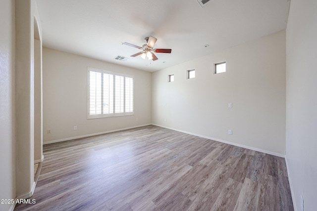 spare room with a ceiling fan, visible vents, arched walkways, wood finished floors, and baseboards