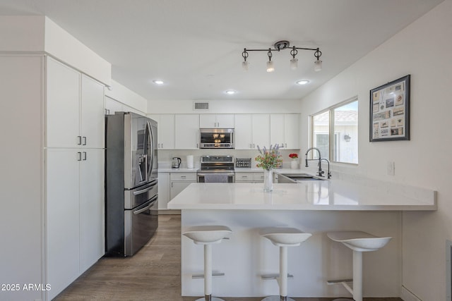 12234 S Pewaukee St, Phoenix, AZ 85044 - kitchen featuring stainless steel appliances, a peninsula, a breakfast bar, wood finished floors, and light countertops