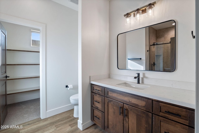 bathroom with toilet, wood finished floors, vanity, baseboards, and a shower stall