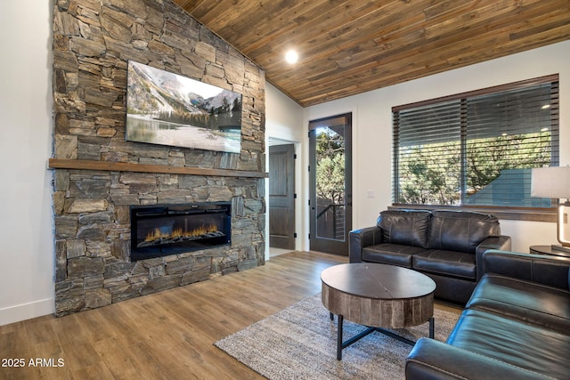 living room featuring baseboards, lofted ceiling, wood ceiling, wood finished floors, and a stone fireplace