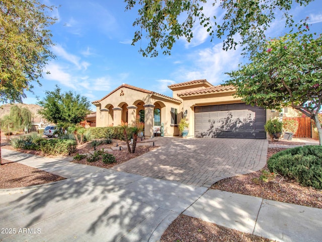 mediterranean / spanish-style home featuring decorative driveway, a tiled roof, an attached garage, and stucco siding