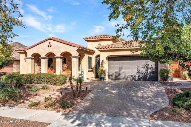 mediterranean / spanish-style house with a garage, decorative driveway, a tiled roof, and stucco siding