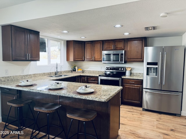 kitchen with appliances with stainless steel finishes, light stone countertops, sink, and light hardwood / wood-style flooring