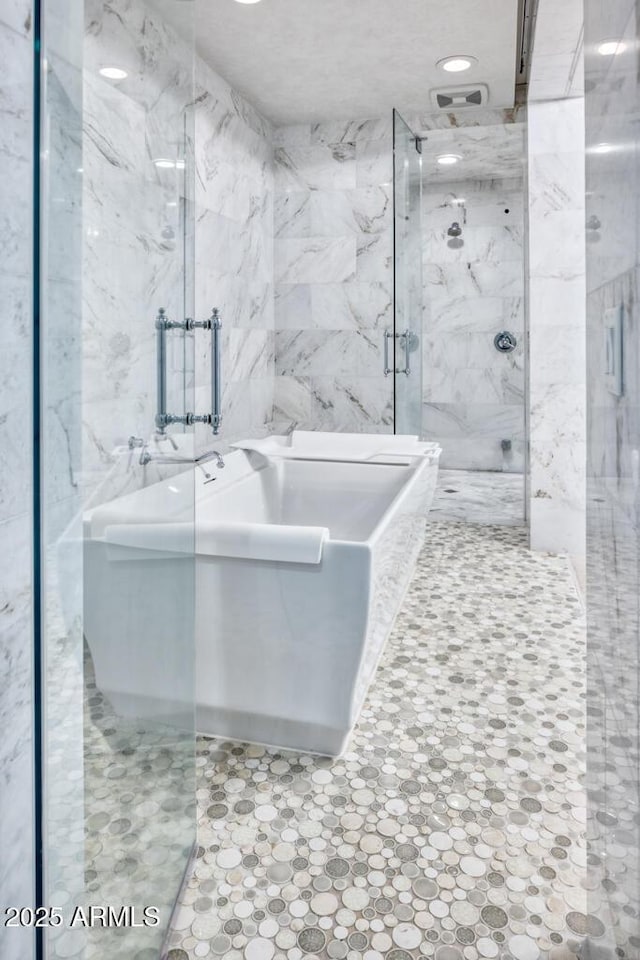 bathroom with a marble finish shower, a freestanding bath, and tile walls