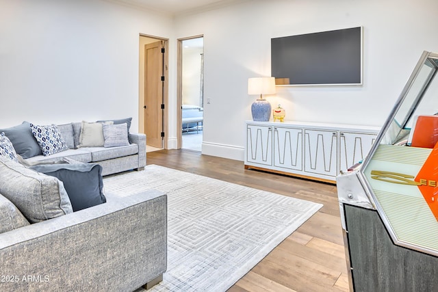 living area with wood finished floors, ornamental molding, and baseboards