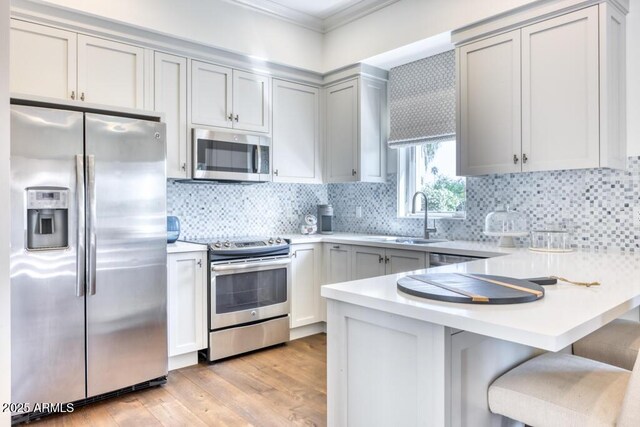 kitchen featuring crown molding, a sink, appliances with stainless steel finishes, light countertops, and a peninsula
