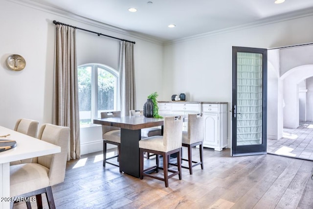 dining room featuring crown molding, light wood-style flooring, recessed lighting, and arched walkways
