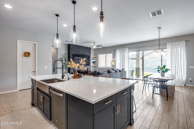 kitchen with light wood-type flooring, decorative light fixtures, a center island with sink, and ceiling fan with notable chandelier