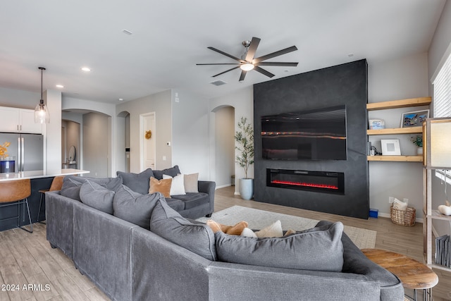 living room with light wood-type flooring, ceiling fan, and a fireplace