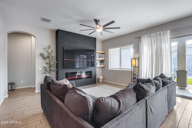 living room featuring ceiling fan, a large fireplace, and light hardwood / wood-style floors