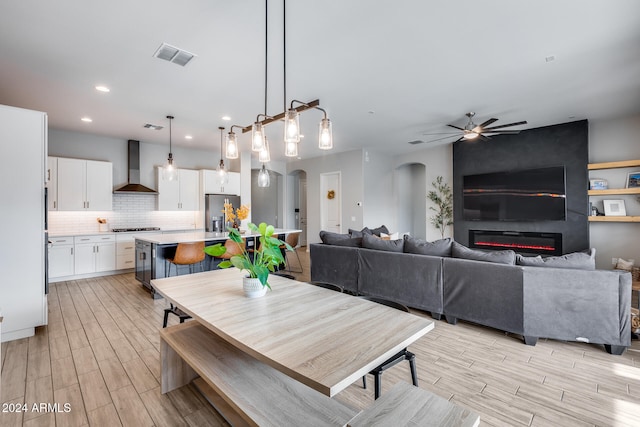 dining area with a large fireplace, ceiling fan, and light hardwood / wood-style flooring