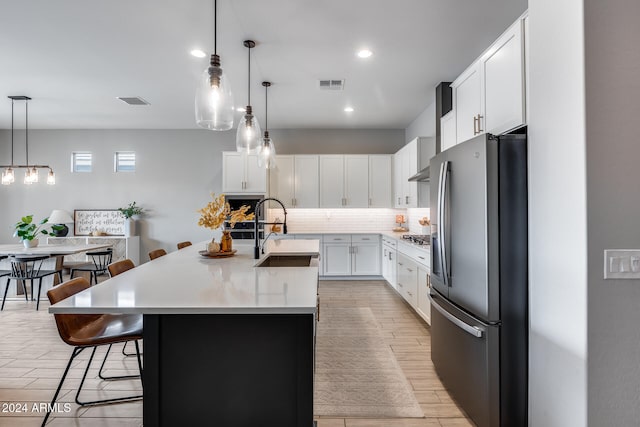 kitchen with a kitchen bar, stainless steel appliances, sink, an island with sink, and white cabinetry