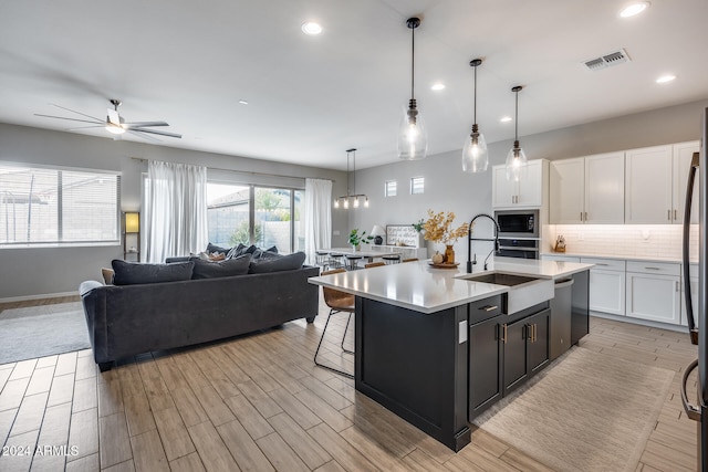 kitchen featuring stainless steel appliances, white cabinetry, sink, decorative light fixtures, and an island with sink