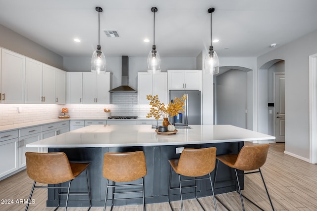 kitchen featuring appliances with stainless steel finishes, a large island, white cabinets, wall chimney exhaust hood, and light hardwood / wood-style flooring