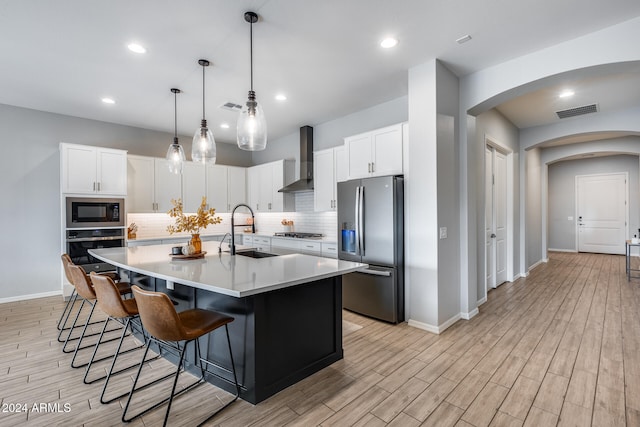 kitchen featuring a center island with sink, stainless steel appliances, white cabinetry, sink, and wall chimney exhaust hood