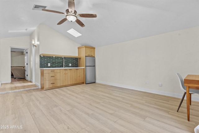 kitchen with tasteful backsplash, visible vents, light wood-style flooring, light brown cabinetry, and freestanding refrigerator