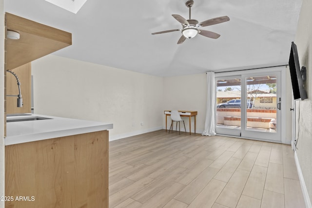 interior space with ceiling fan, vaulted ceiling with skylight, light wood-type flooring, and a sink