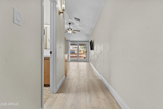 hallway with baseboards, visible vents, a textured wall, and light wood finished floors