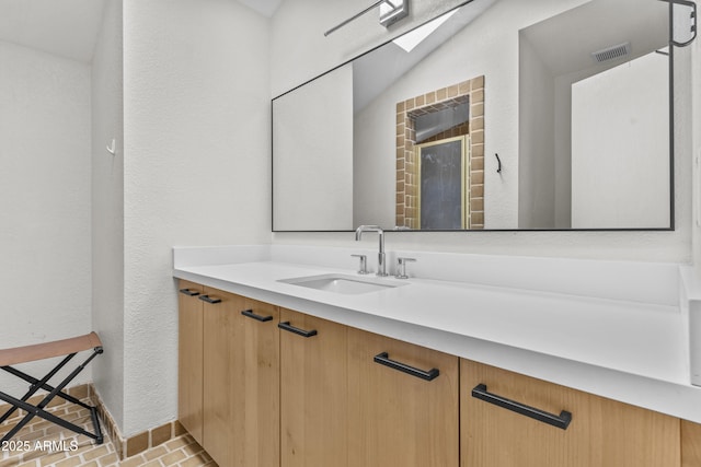 bathroom with a textured wall, brick floor, vanity, and visible vents