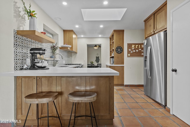 kitchen with a peninsula, a skylight, stainless steel fridge with ice dispenser, decorative backsplash, and open shelves