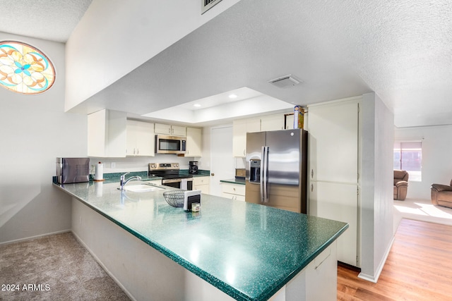 kitchen featuring white cabinetry, kitchen peninsula, appliances with stainless steel finishes, a textured ceiling, and light wood-type flooring