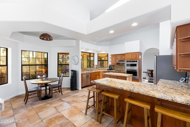 kitchen featuring sink, light stone counters, kitchen peninsula, a breakfast bar area, and appliances with stainless steel finishes