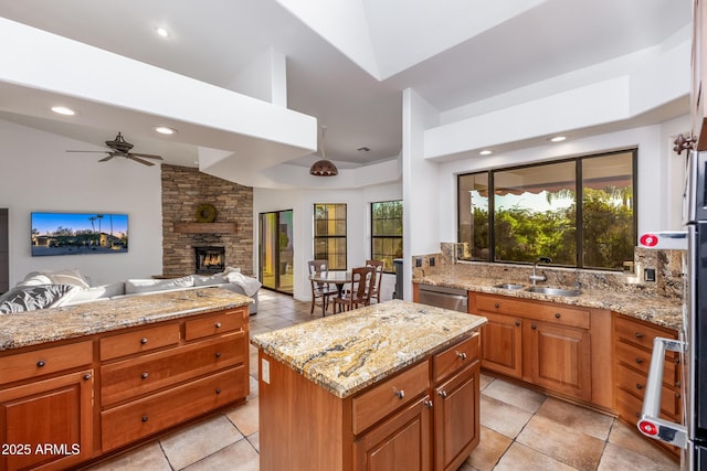 kitchen with light stone countertops, a center island, sink, ceiling fan, and a stone fireplace