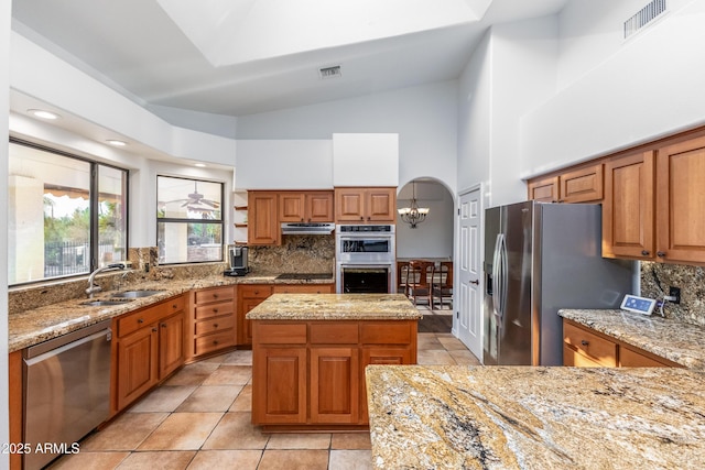 kitchen with light stone counters, a center island, stainless steel appliances, tasteful backsplash, and sink