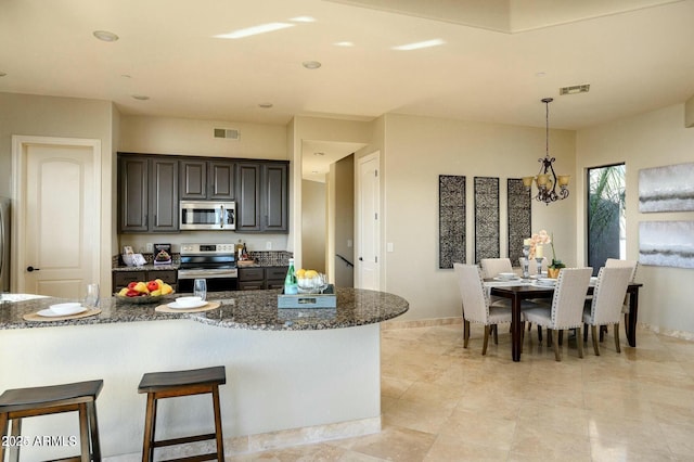 16569 E Trevino Dr, Fountain Hills, AZ 85268 - kitchen with appliances with stainless steel finishes, a chandelier, dark stone counters, pendant lighting, and a kitchen bar